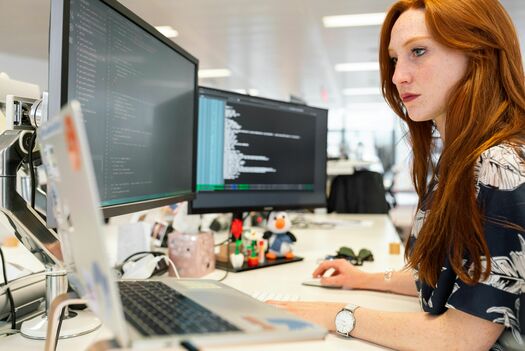 Das Bild zeigt eine Entwicklungsingenieurin, die vor zwei Bildschirmen sitzt und etwas ausarbeitet.