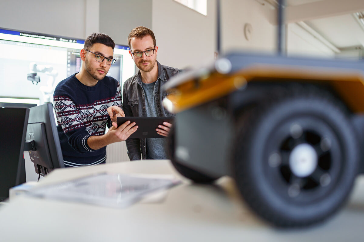 Ein Studierender und ein Mitarbeiter aus dem Fachbereich Elektrotechnik/Ingenieurinformatik sind im Robotiklabor der Hochschule und steuern einen fahrenden Roboter von Ferne. 