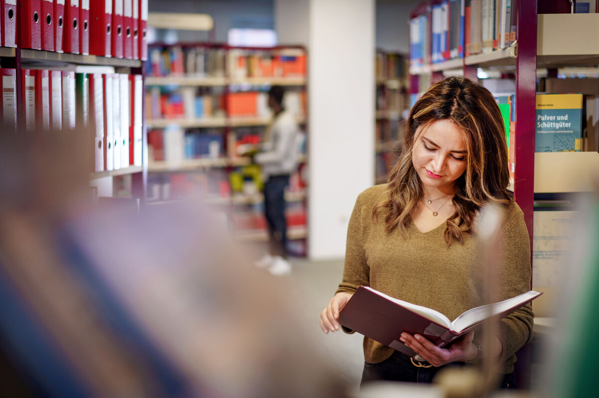 Eine Studentin steht in der Bibliothek der THGA und liest ein Buch über Ingenieurwesen.
