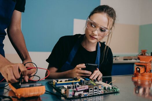 Das Bild zeigt eine Hardware Ingenieurin. Sie lötet an einem Hardware-Gerät und trägt eine Schutzbrille.