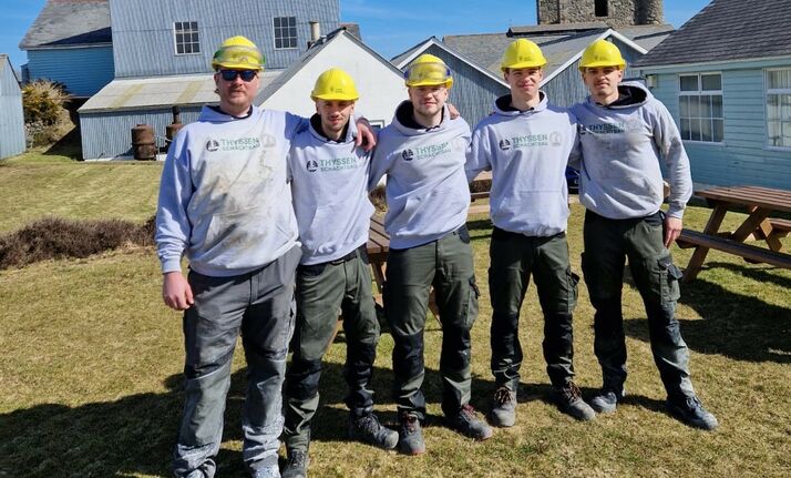Sechs Teammitglieder sind Studierende der THGA und stehen als Gruppe in der Mitte des Fotos. Sie tragen Schutzhelme.