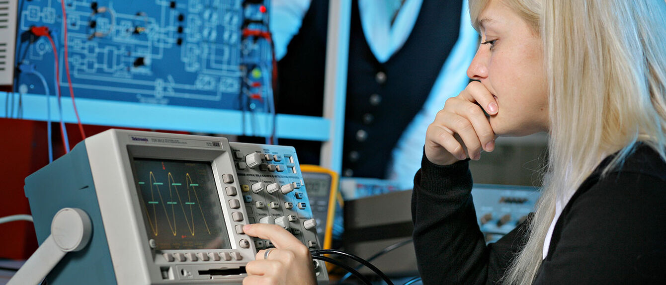 Eine Frau bedient ein technisches Messgerät im Labor Bachelor Elektrotechnik.