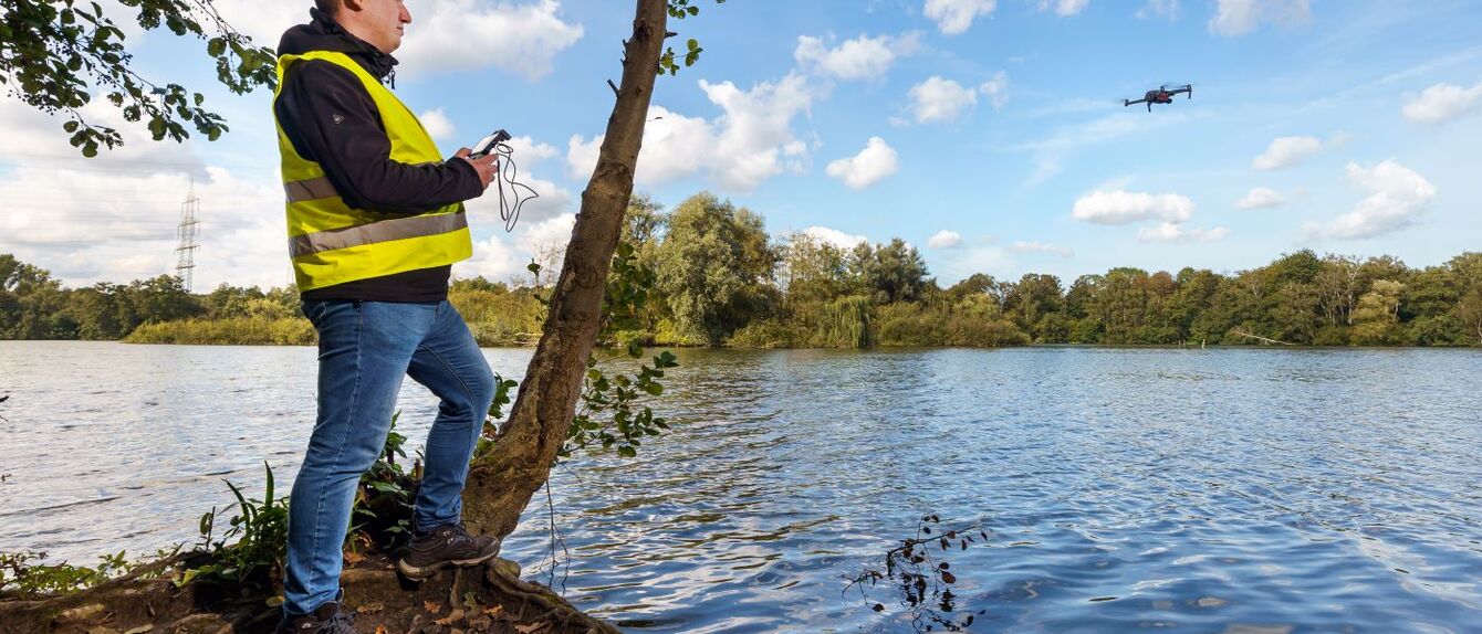 Wissenschaftler steht an einem Bergsenkungssee und überwacht mit einer Drohne die Umwelt. 