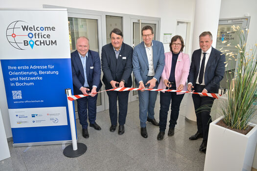 Zu sehen sind fünf Personen, die ein symbolisches Band für die Eröffnung des Büros durchschneiden. 