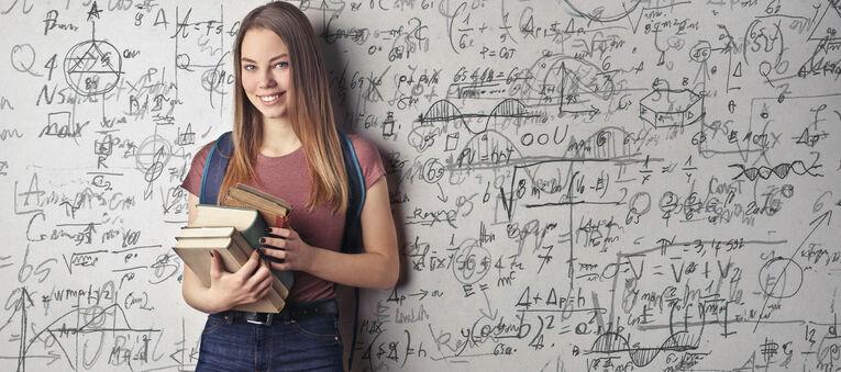 Eine junge Frau steht vor einer Tafel mit mathematischen Gleichungen.