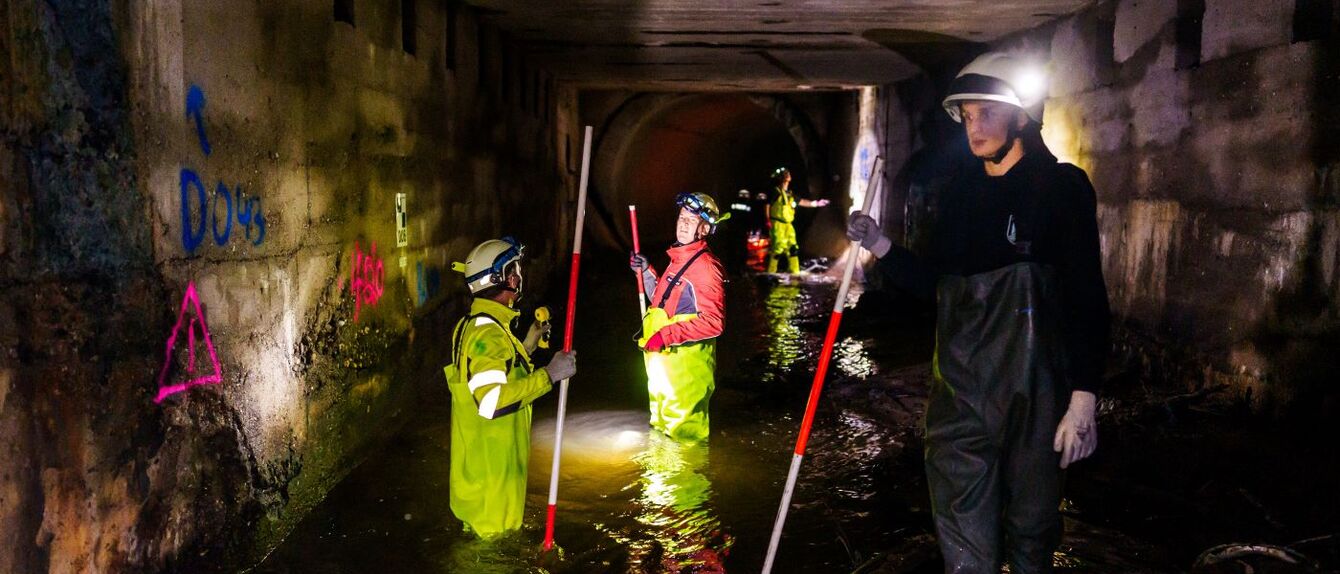 Zu sehen sind drei Wissenschaftler, davon einer mit einem Messgerät im Vordergrund. Sie vermessen und prüfen die Bausubstanz des Passbachtunnels im Ruhrgebiet. 